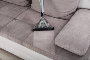 Closeup Of Cleaning Sofa With Vacuum Cleaner At Home